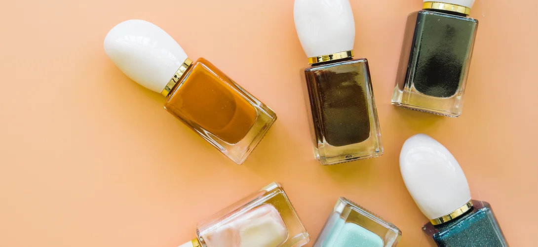 Gel polish bottles in bronze, olive, teal and pastel shades laid out on a peach background